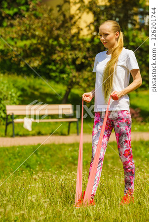 Girl doing exercises outdoor, using resistance fit band. 126201744