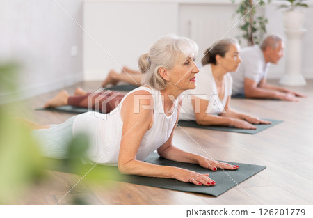 Mature women of different year practice yoga and Pilates in virabhadrasana pose in gym Mature women of different year practice yoga and Pilates in virabhadrasana pose in gym 126201779