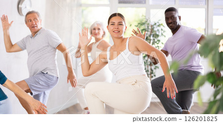 Young teacher and group of positive aged people engaged in dynamic dances 126201825