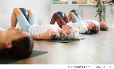 Mature woman doing exercises with pilates ball during group training at gym indoor 126201924