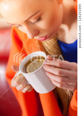 Woman lying on sofa under blanket drinking tea Woman lying on sofa under blanket drinking tea 126201995