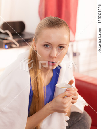 Woman lying on sofa under blanket drinking tea Woman lying on sofa under blanket drinking tea 126201996