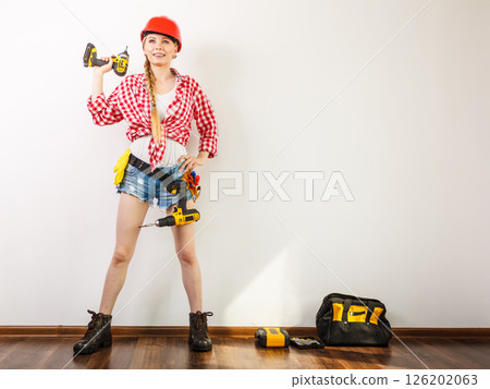 Woman wearing helmet, toolbelt about to drill wall Woman wearing helmet, toolbelt about to drill wall 126202063