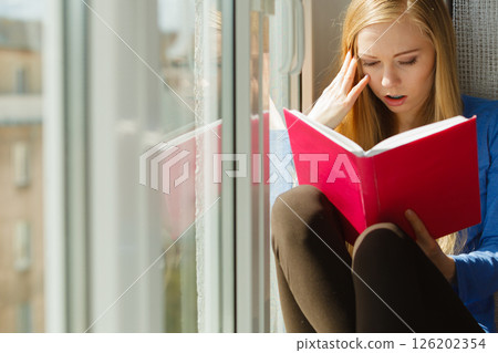 Woman reading on windowsill Woman reading on windowsill 126202354