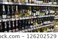 rows of wine bottles on shelves, blurred image of wine bottled on the shelf in supermarket. grocery store display wine and liquor defocus, no people. 126202529