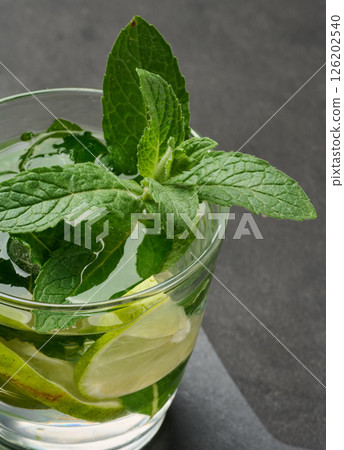 Refreshing mojito cocktail with lime, mint, strawberry, and ice on dark background, top view Refreshing mojito cocktail with lime, mint, strawberry, and ice on dark background, top view 126202540