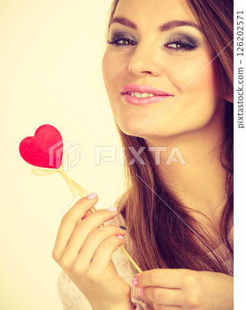 Flirty woman holding red wooden heart on stick Flirty woman holding red wooden heart on stick 126202571