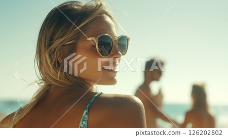 Woman enjoys a sunny day at the beach with sunglasses, smiling enigmatically while turning her head left 126202802