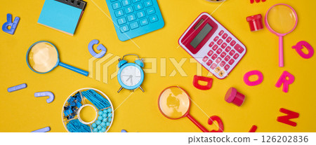 Colorful school supplies, learning items calculators, letters, tools, and stationery scattered on a vibrant yellow background. 126202836