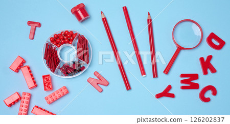 Flat lay of red stationery, learning items letters, magnifying glass, supplies, bricks, toys, and alarm clock on a light blue background. 126202837