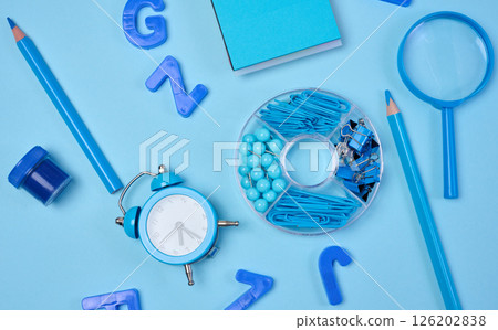 Flat lay of blue stationery, learning items letters, magnifying glass, supplies, and an alarm clock on a blue background. Education, time, and study concept 126202838