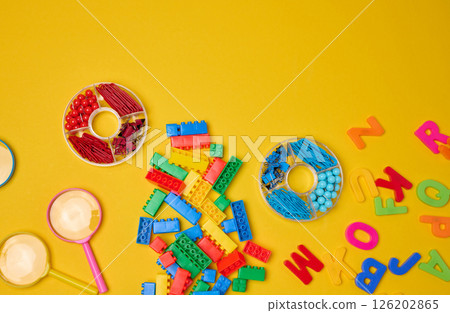 Collection of colorful school supplies, building bricks, letters, and learning items scattered on a yellow background. 126202865