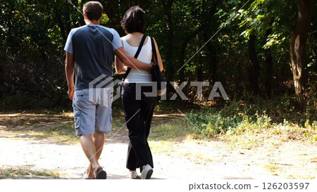 Happy couple walking along path at summer forest. Romantic pair going along trail at wild woodland. Lovers spending time together at nature. Concept of love and happiness. Slow motion Happy couple walking along path at summer forest. Romantic pair going along trail at wild woodland. Lovers spending time together at nature. Concept of love and happiness. Slow motion 126203597