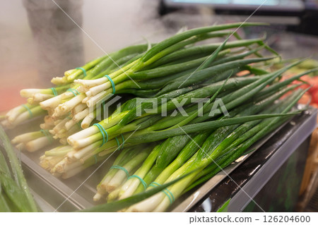A bunch of green onions are on a table. The onions are wet and have plastic ties wrapped around them A bunch of green onions are on a table. The onions are wet and have plastic ties wrapped around them 126204600