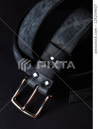 A black belt with a silver buckle sits on a black background. The belt is made of leather and has a gold buckle A black belt with a silver buckle sits on a black background. The belt is made of leather and has a gold buckle 126204607