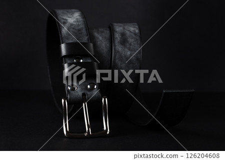 A black belt with a silver buckle is laying on a black surface. The belt is made of leather and has a silver buckle A black belt with a silver buckle is laying on a black surface. The belt is made of leather and has a silver buckle 126204608