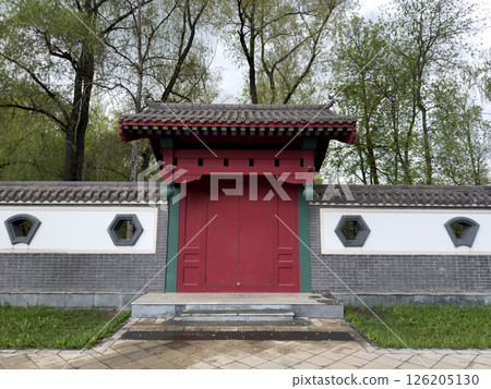 Traditional red wooden gate with tiled roof and geometric windows in decorative wall, inspired by East Asian architecture. Symmetry design and natural park background make. Ideal for visual projects Traditional red wooden gate with tiled roof and geometric windows in decorative wall, inspired by East Asian architecture. Symmetry design and natural park background make. Ideal for visual projects 126205130