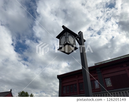 Traditional black and white lantern on a tall post stands in front of red Chinese style building with decorative windows and cloudy sky, emphasizing cultural design and symmetry 126205149