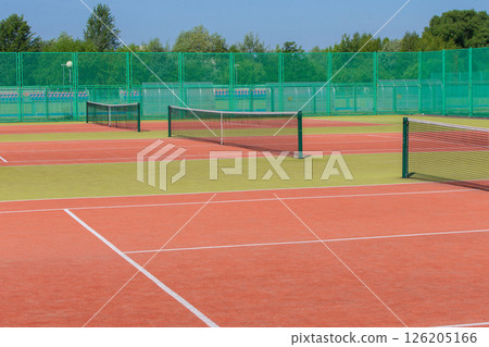 The tennis court is empty with a net and a green fence. The tennis court is empty with a net and a green fence. 126205166