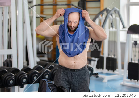 A man in the gym puts on a blue T-shirt after a workout. A man in the gym puts on a blue T-shirt after a workout. 126205349