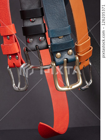 Various leather belts with metal buckles close-up on dark grey background. Various leather belts with metal buckles close-up on dark grey background. 126205371