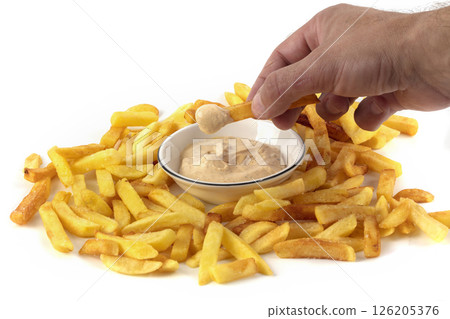 A hand dips French fries into a white bowl of sauce. A hand dips French fries into a white bowl of sauce. 126205376