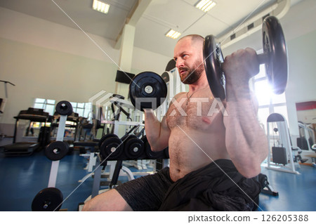 A man lifts weights in a gym equipped with various machines and weights 126205388