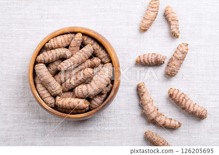 Fresh turmeric rhizomes in a wooden bowl on linen. Underground stems of the turmeric plant Curcuma longa, with bright orange flesh. Used fresh, or dried and ground as turmeric powder. Food photo. Fresh turmeric rhizomes in a wooden bowl on linen. Underground stems of the turmeric plant Curcuma longa, with bright orange flesh. Used fresh, or dried and ground as turmeric powder. Food photo. 126205695