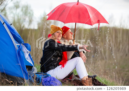 Elderly couple sitting under umbrella near tourist tent in rain. Travel of elderly man and woman in nature. Elderly couple sitting under umbrella near tourist tent in rain. Travel of elderly man and woman in nature. 126205989