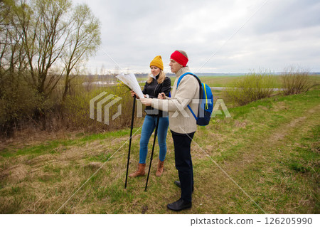 Active elderly Caucasian couple hiking with backpacks and hiking poles enjoying their adventure. They are looking at a map or a tourist route. 126205990