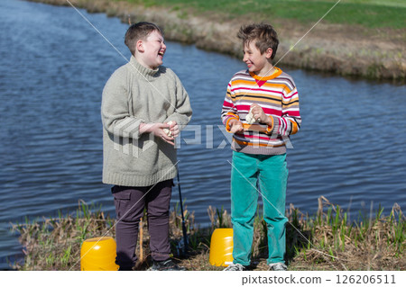 Two boys on a fishing trip are preparing fish bait from dough. They are chatting and laughing. 126206511