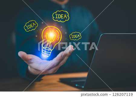 Person presenting a glowing lightbulb icon and "idea" text bubbles, symbolizing creative ideas and innovation, while the person works on a laptop, representing brainstorming and technology. 126207119