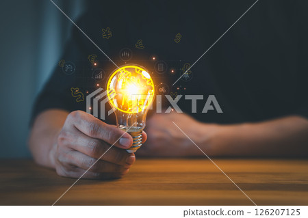 A person holds a glowing light bulb surrounded by currency symbols and business icons, symbolizing innovation, financial ideas, and creative solutions in business and technology. A person holds a glowing light bulb surrounded by currency symbols and business icons, symbolizing innovation, financial ideas, and creative solutions in business and technology. 126207125