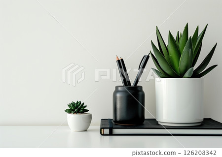 Front view white desk with black stationery, succulent plant, notebook, eyeglasses. Morning background banner, space for text. Minimalistic concept, workspace, time to work. Blank workplace. Mock-up. 126208342