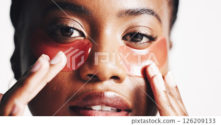 Black woman, portrait and eye patches with mask or hydration on a white studio background. Face, female person or model with facial gel or cosmetics for collagen, dermatology or anti aging treatment Black woman, portrait and eye patches with mask or hydration on a white studio background. Face, female person or model with facial gel or cosmetics for collagen, dermatology or anti aging treatment 126209133