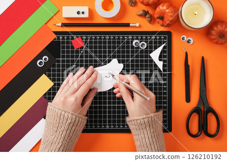 Making a ghost toy out of paper. Cut out the arms with a paper knife. Around accessories for creativity from paper, cutting mat, scissors, tweezers, tape. Making a ghost toy out of paper. Cut out the arms with a paper knife. Around accessories for creativity from paper, cutting mat, scissors, tweezers, tape. 126210192