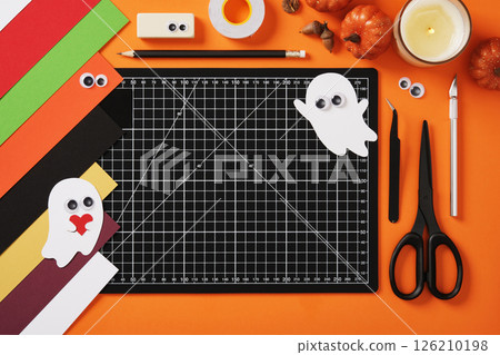 Paper crafts for halloween ghosts. Finished crafts on a background of diy art supplies. Cutting mat, scissors, cutter, tweezers, pencil, eraser, tape, paper. Space for your text. Paper crafts for halloween ghosts. Finished crafts on a background of diy art supplies. Cutting mat, scissors, cutter, tweezers, pencil, eraser, tape, paper. Space for your text. 126210198