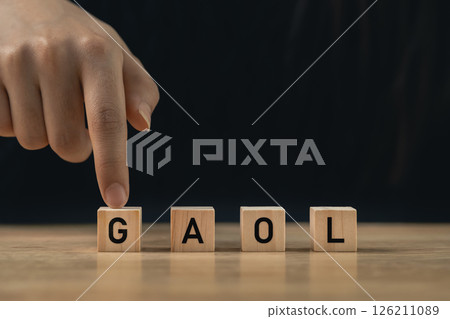 Wooden blocks spelling out the word "GAOL" with a hand pointing, showcasing creativity and learning, ideal for educational or motivational themes. 126211089