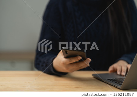Person using smartphone and laptop on wooden table with cozy atmosphere for remote work or digital communication concept Person using smartphone and laptop on wooden table with cozy atmosphere for remote work or digital communication concept 126211097