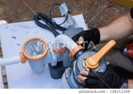 Individual is connecting parts of water pump to pool filter in outdoor setting 126211269