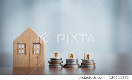 Wooden house model and coin stack with TAX word on wooden table. Wooden house model and coin stack with TAX word on wooden table. 126211272