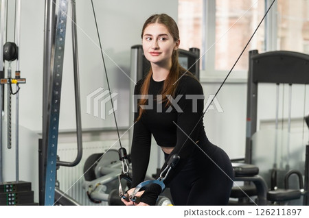 Fit young woman training with cable crossover machine indoors. 126211897