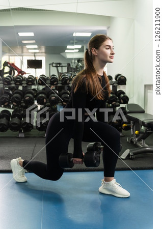 Young woman doing dumbbell lunges in modern gym. Young woman doing dumbbell lunges in modern gym. 126211900