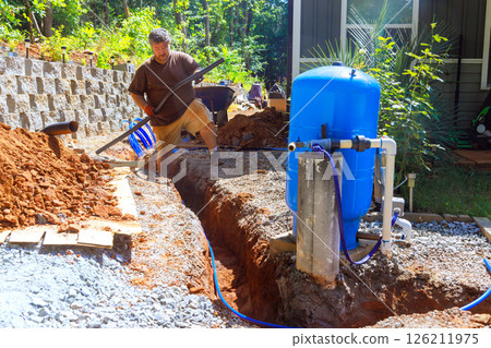 Worker actively pipe PEX laying to trench for artesian water well system installation 126211975