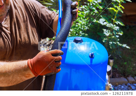 Contractor in gloves is fixing artesian water well pump at home, inspecting black hose 126211978