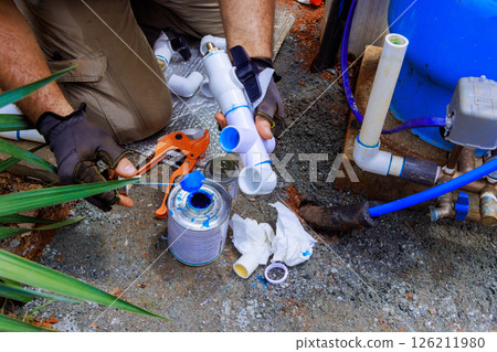 Worker fixes plumbing in artesian water using tools surrounded by pvc pipes, equipment. 126211980