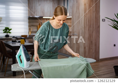 Ironing clothes in a cozy modern kitchen space during a sunny day 126212129