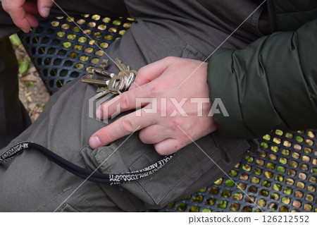 The man sits on a metal bench and holds iron key in the hand. 126212552