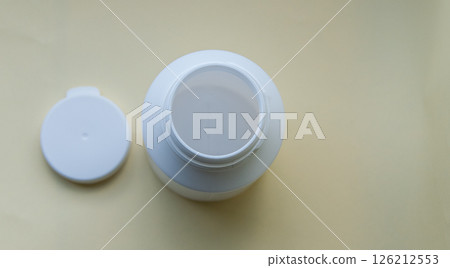 Open white bottle for pills on the yellow nature background. Farmacy concept. Flat lay. Copy space. Space for text. Open white bottle for pills on the yellow nature background. Farmacy concept. Flat lay. Copy space. Space for text. 126212553