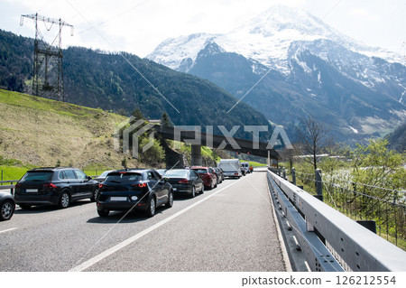 A lot of cars stay in traffic jam on the road near tunnel with mountains and forest in Switzerland. 126212554